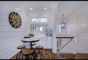Cozy interior with table, stools, clock, staircase, window, mirror, and lantern light.